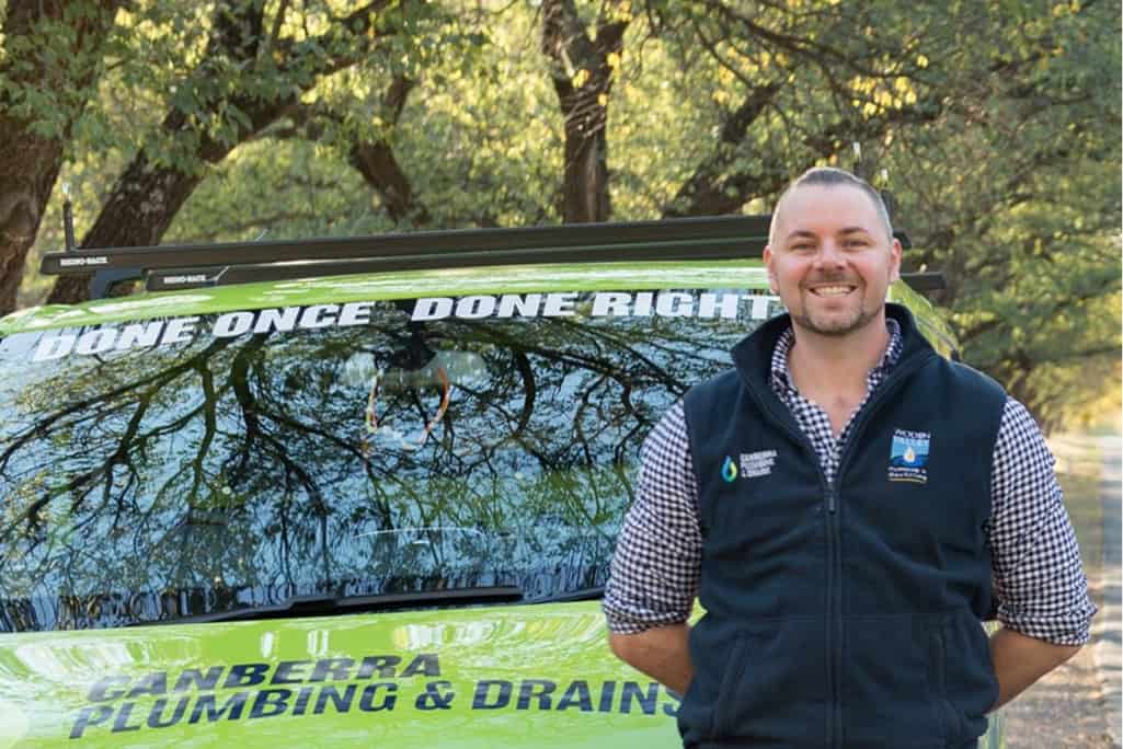 Plumber in front of Canberra Plumbing & Drains service vehicle outdoors.